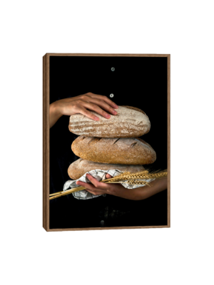 Imagem de um quadro que mostra uma mulher segurando três pães rústicos empilhados, com uma textura áspera e castanho claro. Na outra mão, ela segura um feixe de trigo. O fundo preto destaca o contraste entre o pão e o trigo dourado.