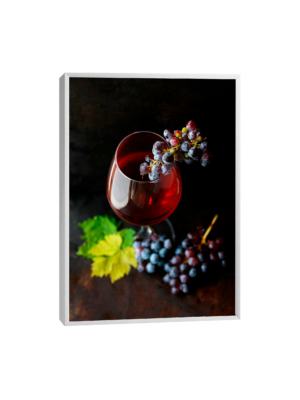 Quadro que retrata uma taça de vinho tinto em cristal sobre uma mesa de madeira rústica, acompanhada por cachos de uvas roxas e folhas verdes, evocando sofisticação e charme.